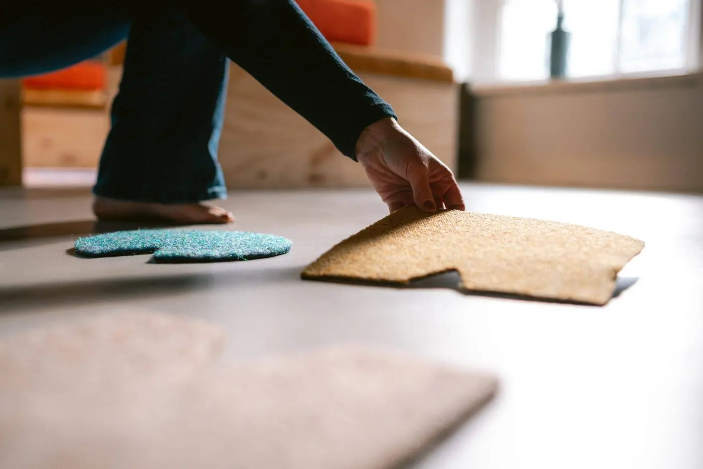 Een hand zet een gekleurde vorm op de vloer, tussen andere vormen, in zacht licht